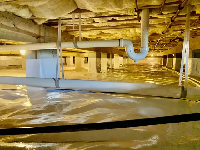 Encapsulated Hampton Roads crawl space with a reinforced vapor barrier sealed across the ground and up the piers, insulated joists overhead, and lit, dry access between the drain lines